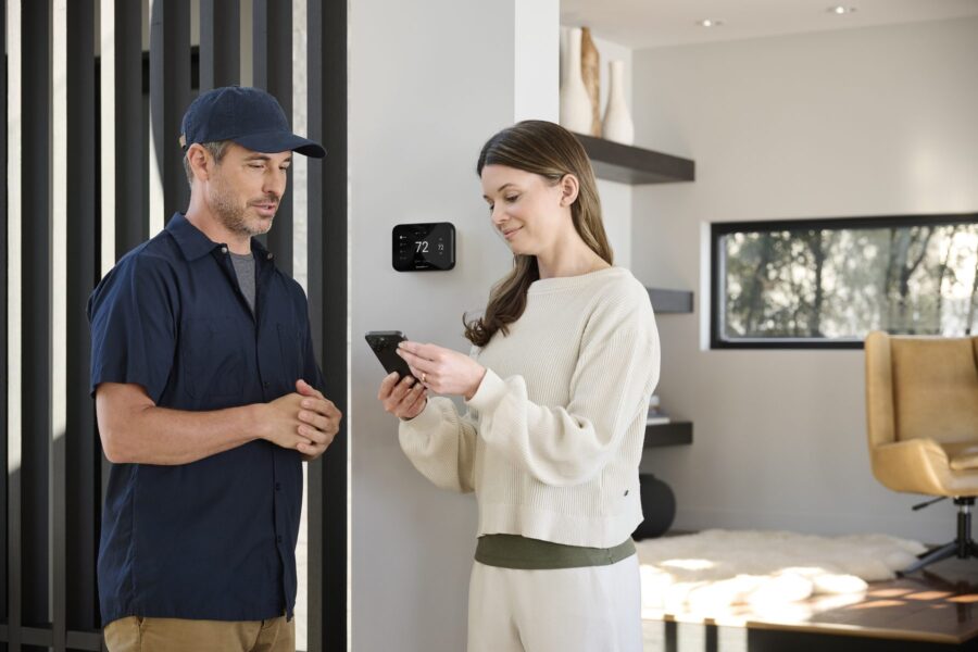 An HVAC technician and a homeowner set up a Honeywell Home thermostat with a phone